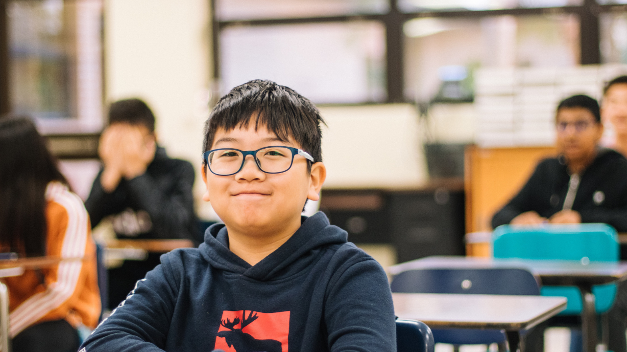 Young boy in classroom with glasses smiling