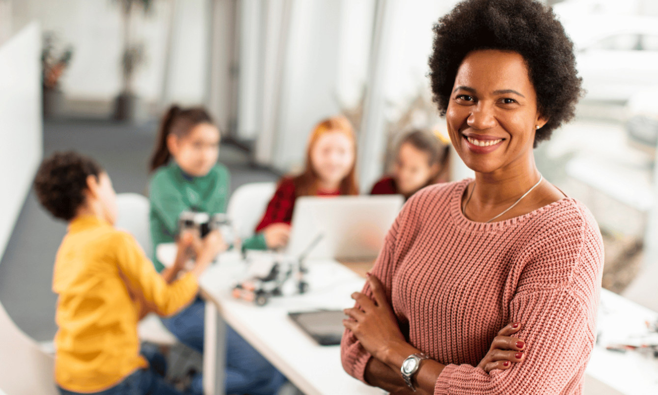 Smiling teacher of color with kids working in the background